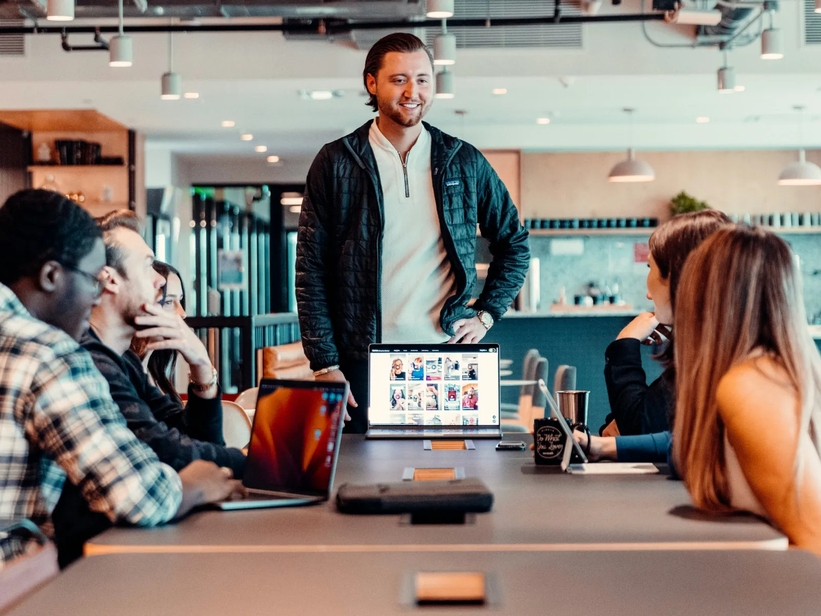 Young man leading a team meeting in modern office with laptops and digital tablet on table