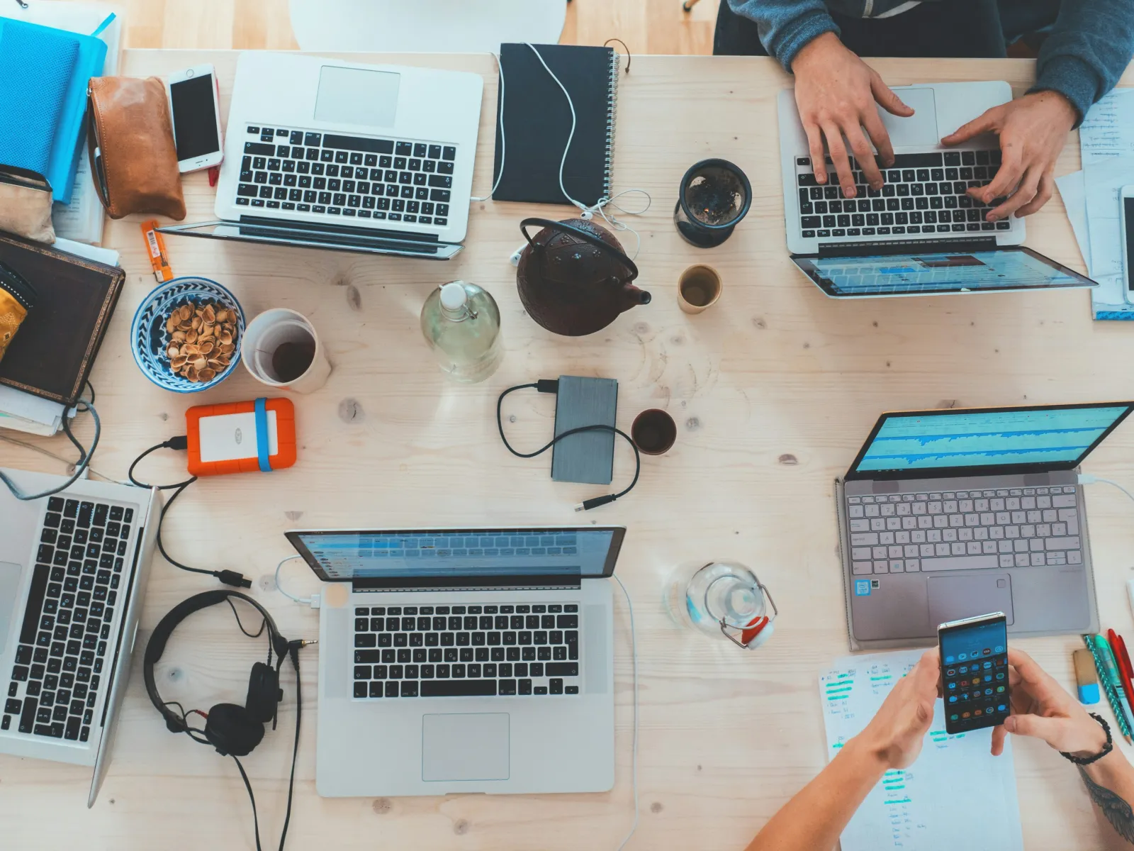 Overhead view of a collaborative workspace with multiple laptops and devices on a wooden table.