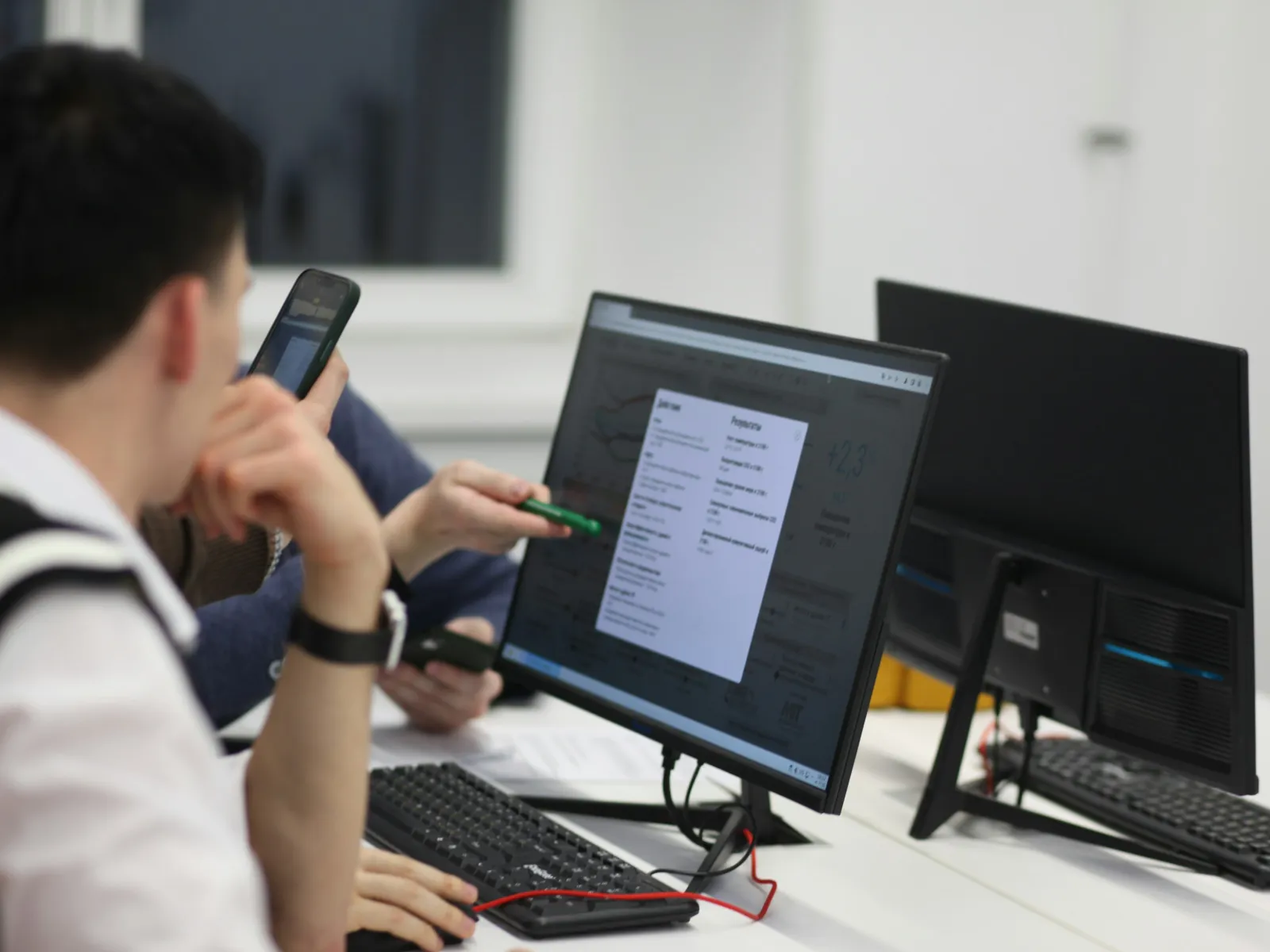 Two colleagues analyze data on a desktop monitor discussing business insights in a modern office.