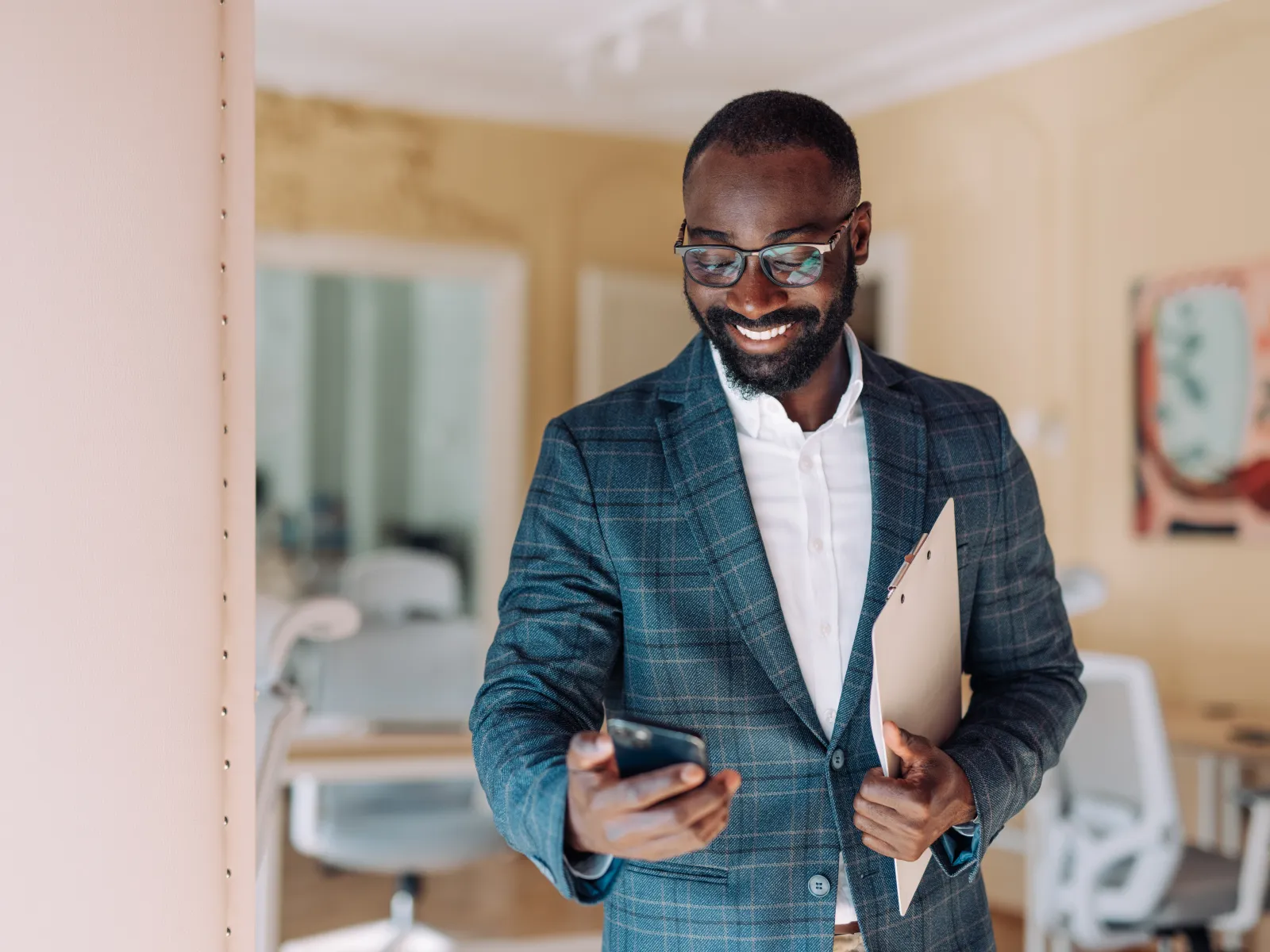 Smiling businessman in checkered suit holding clipboard and smartphone in modern office setting