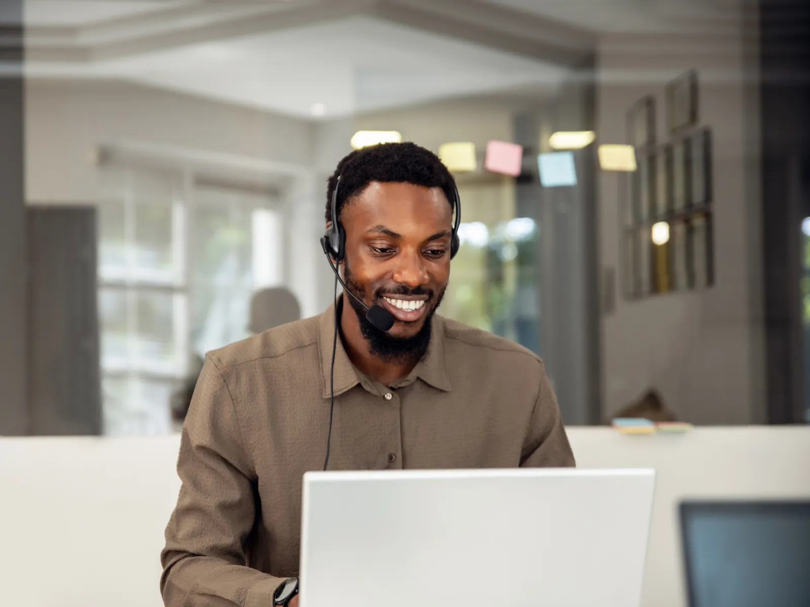Customer service team working at computers wearing headsets in a bright modern office with large windows.