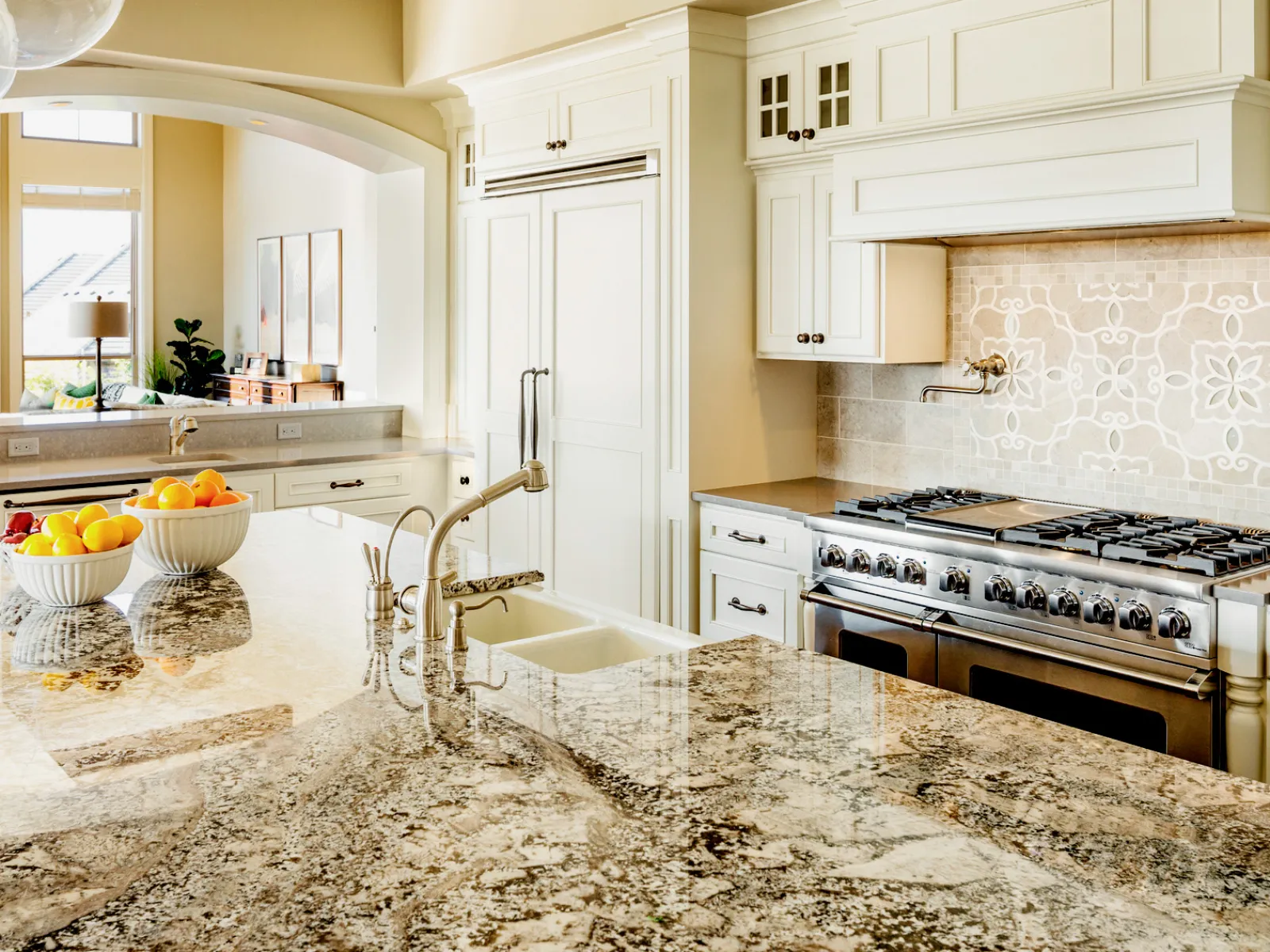 Bright kitchen with granite countertops, white cabinetry, modern stainless steel stove, and decorative backsplash.