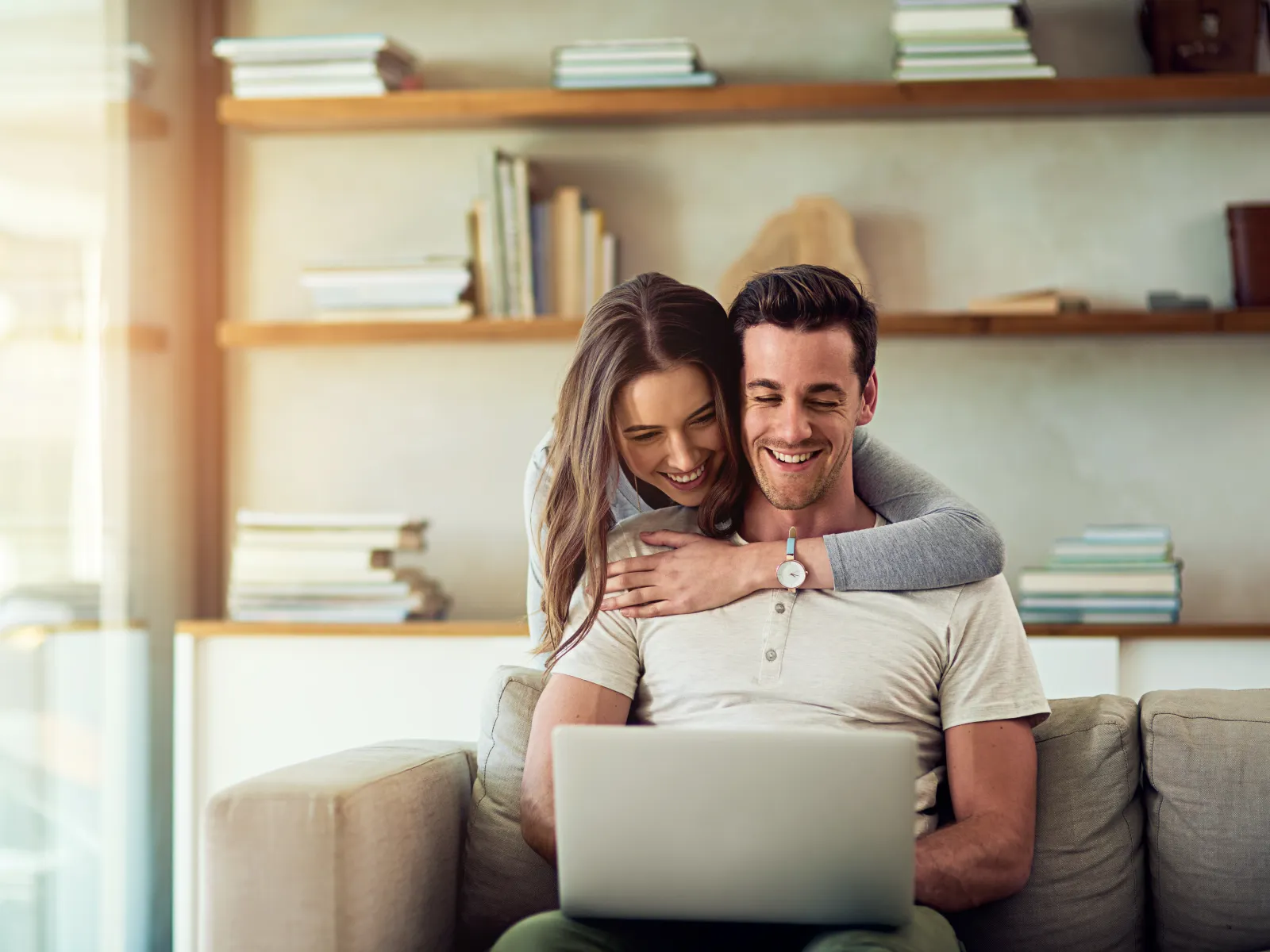 Happy couple using laptop together on couch in cozy living room with bookshelves in background