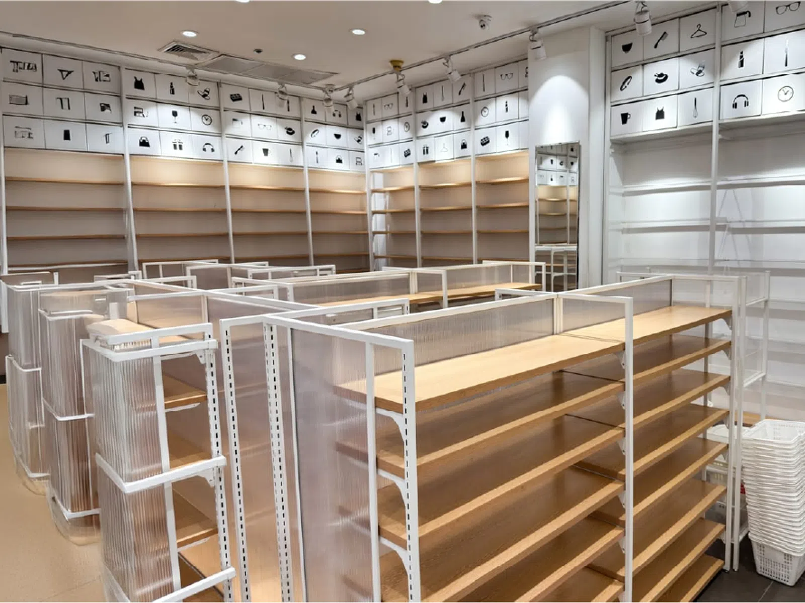 Empty retail store with wooden shelves and white metal racks under bright lighting and icon labels on walls.