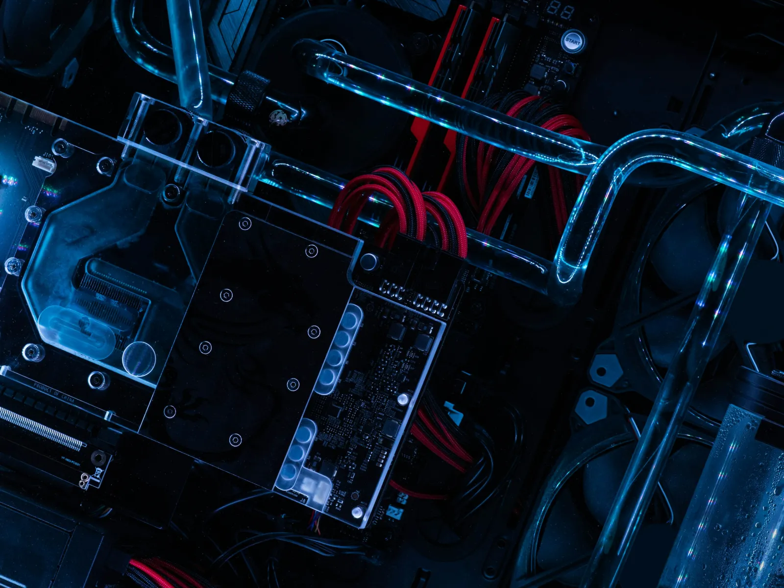 Close-up of a custom water-cooled PC build with transparent tubes and red power cables illuminated by blue light.