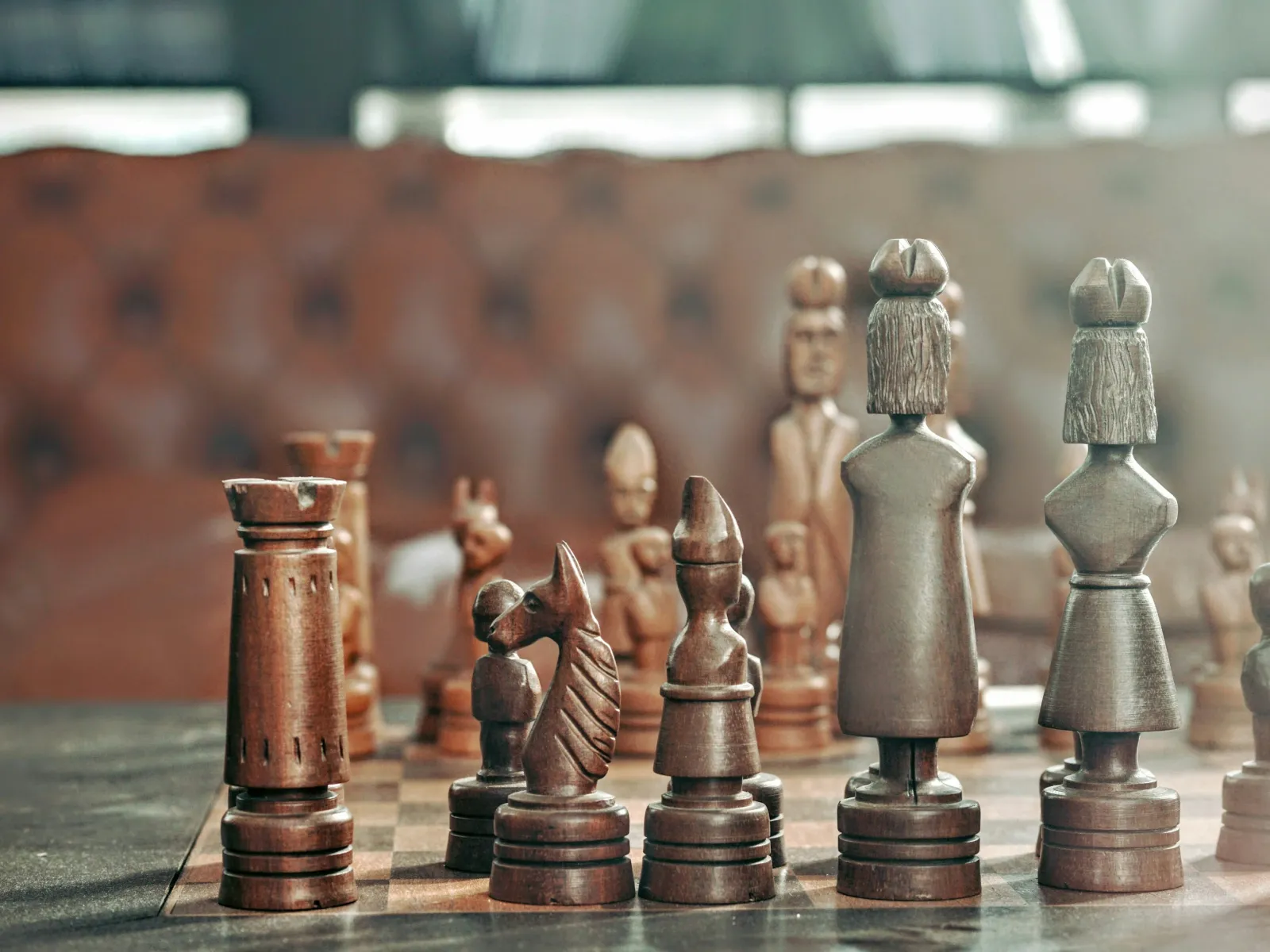 Close-up of intricately carved wooden chess pieces arranged on a board in a cozy room setting.