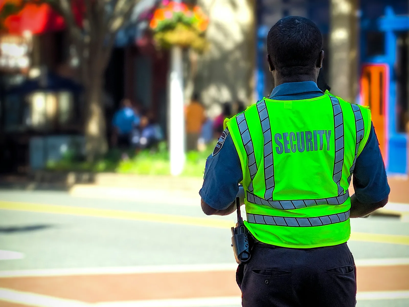 Security guard in fluorescent vest standing on a city street during daytime with blurred background of shops and trees