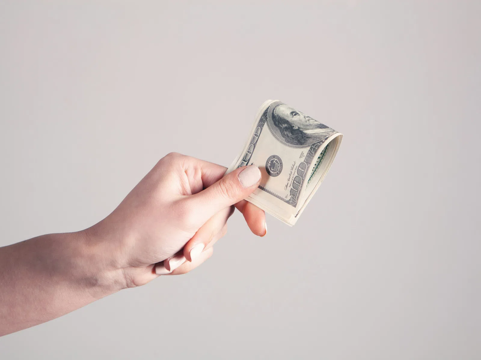 Hand holding a folded 100 dollar bill against a plain light background