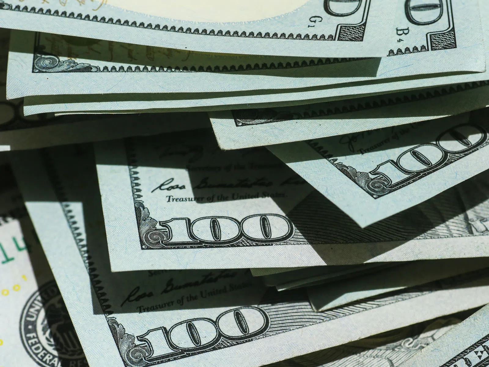 Pile of US hundred dollar bills with clear denominations and security features in natural light.