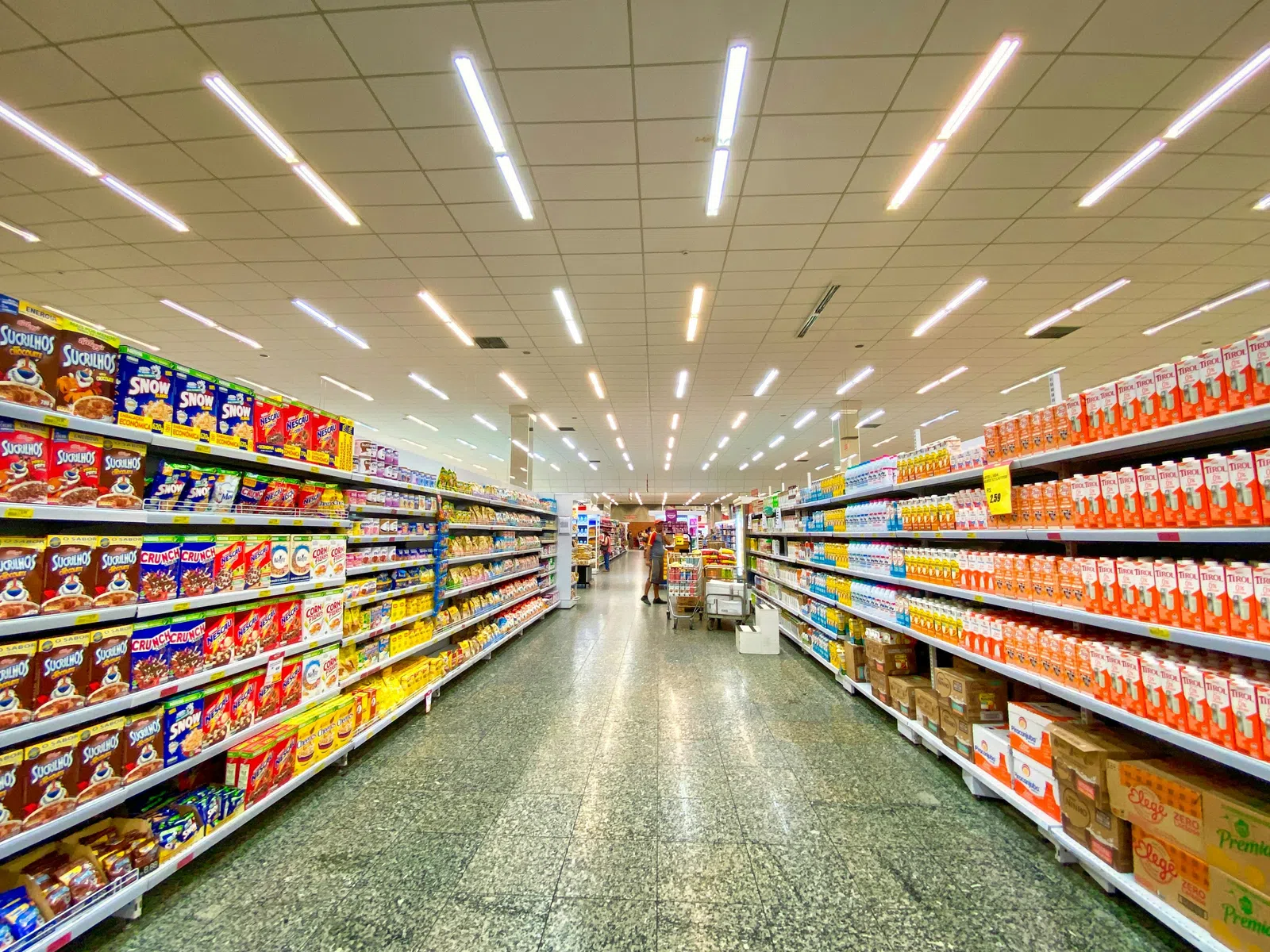Supermarket aisle stocked with colorful cereal boxes and juice cartons under bright LED lights.
