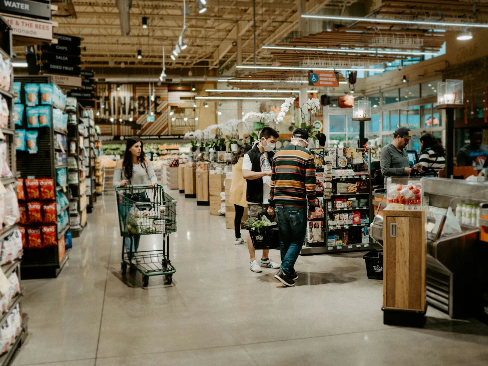 Customers shopping and checking out groceries inside a modern supermarket with well-lit aisles and stocked shelves.