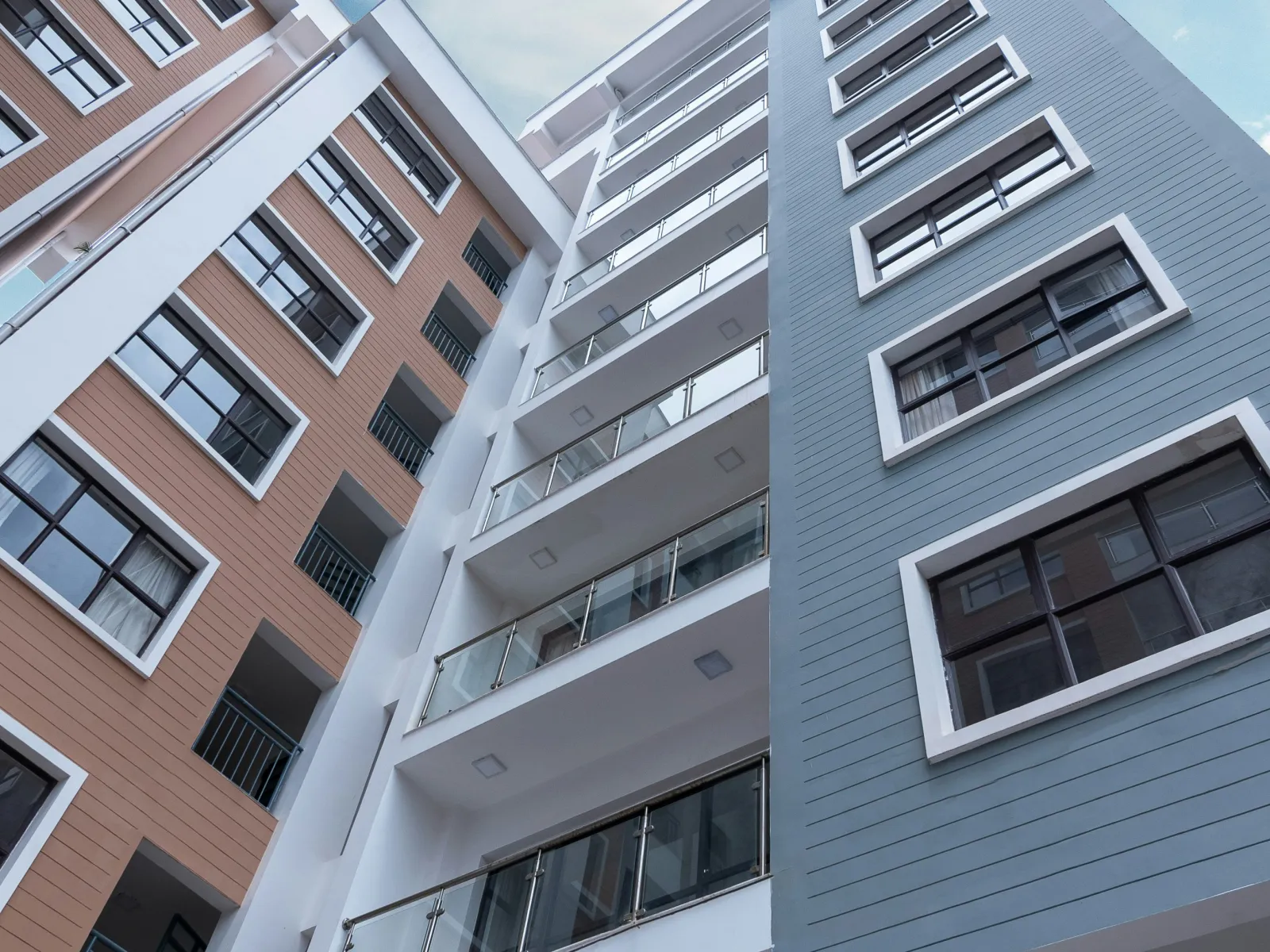 Modern multi-story residential buildings with balconies under a partly cloudy blue sky.