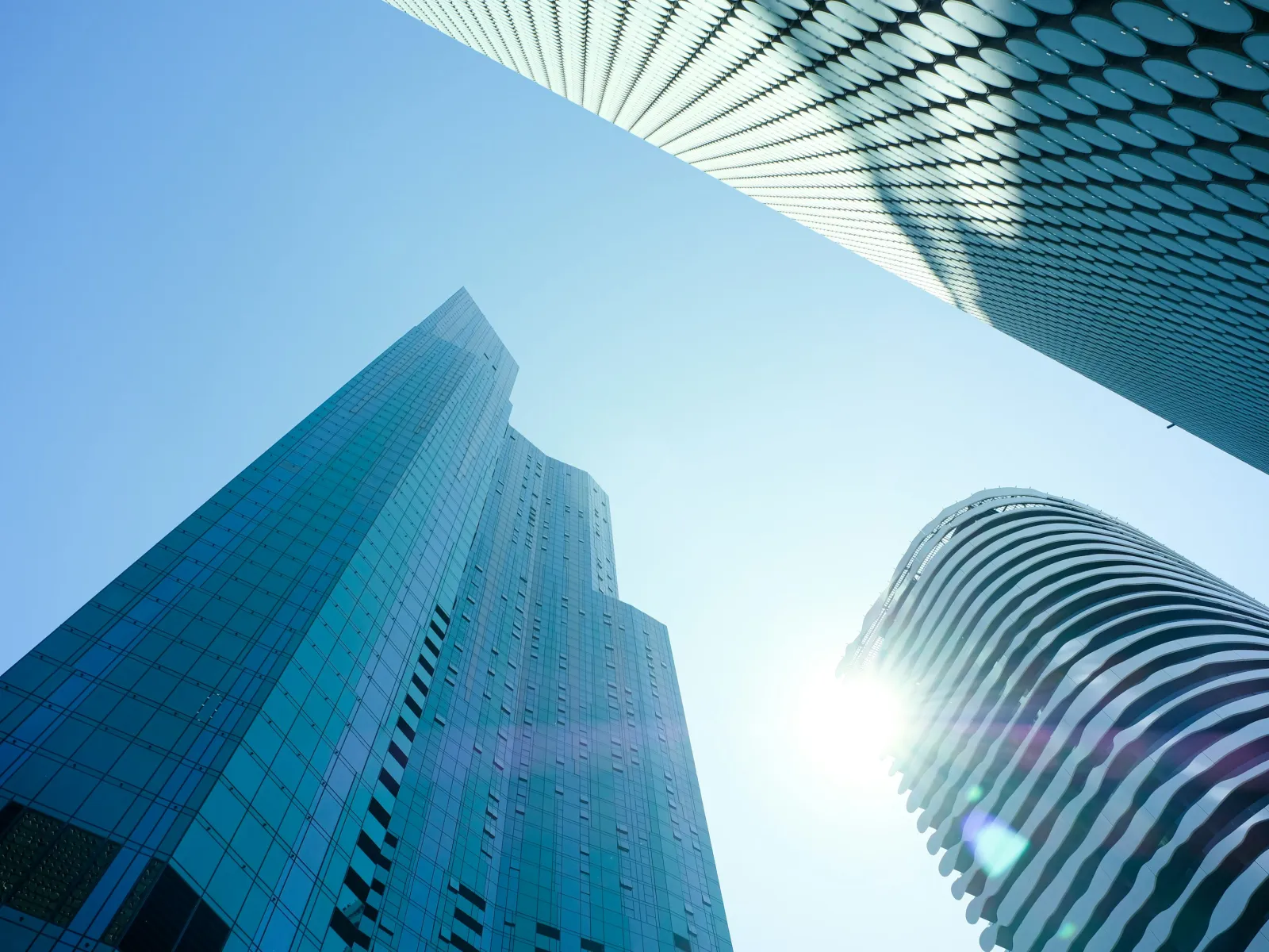 Low angle view of modern skyscrapers with glass facades and bright sun in clear blue sky background