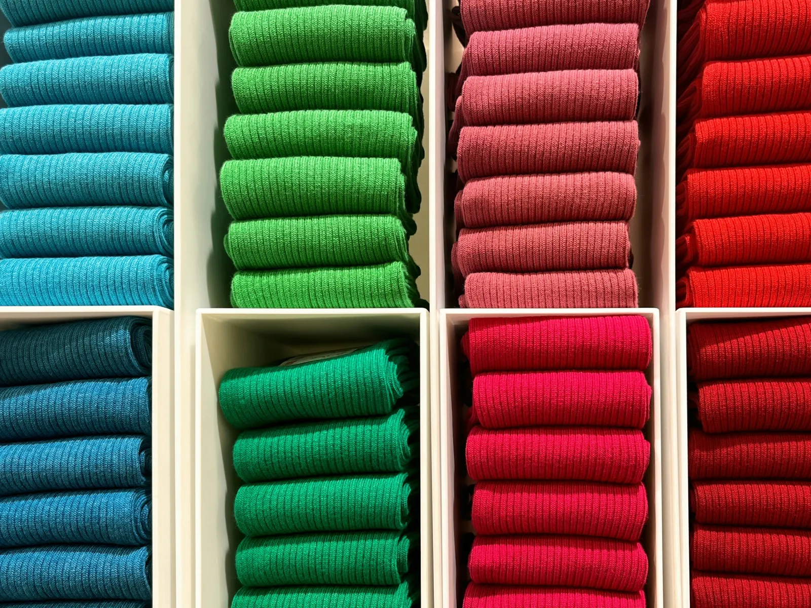 Neatly folded sweaters in vibrant blue, green, pink, and red colors organized in separate white shelves.
