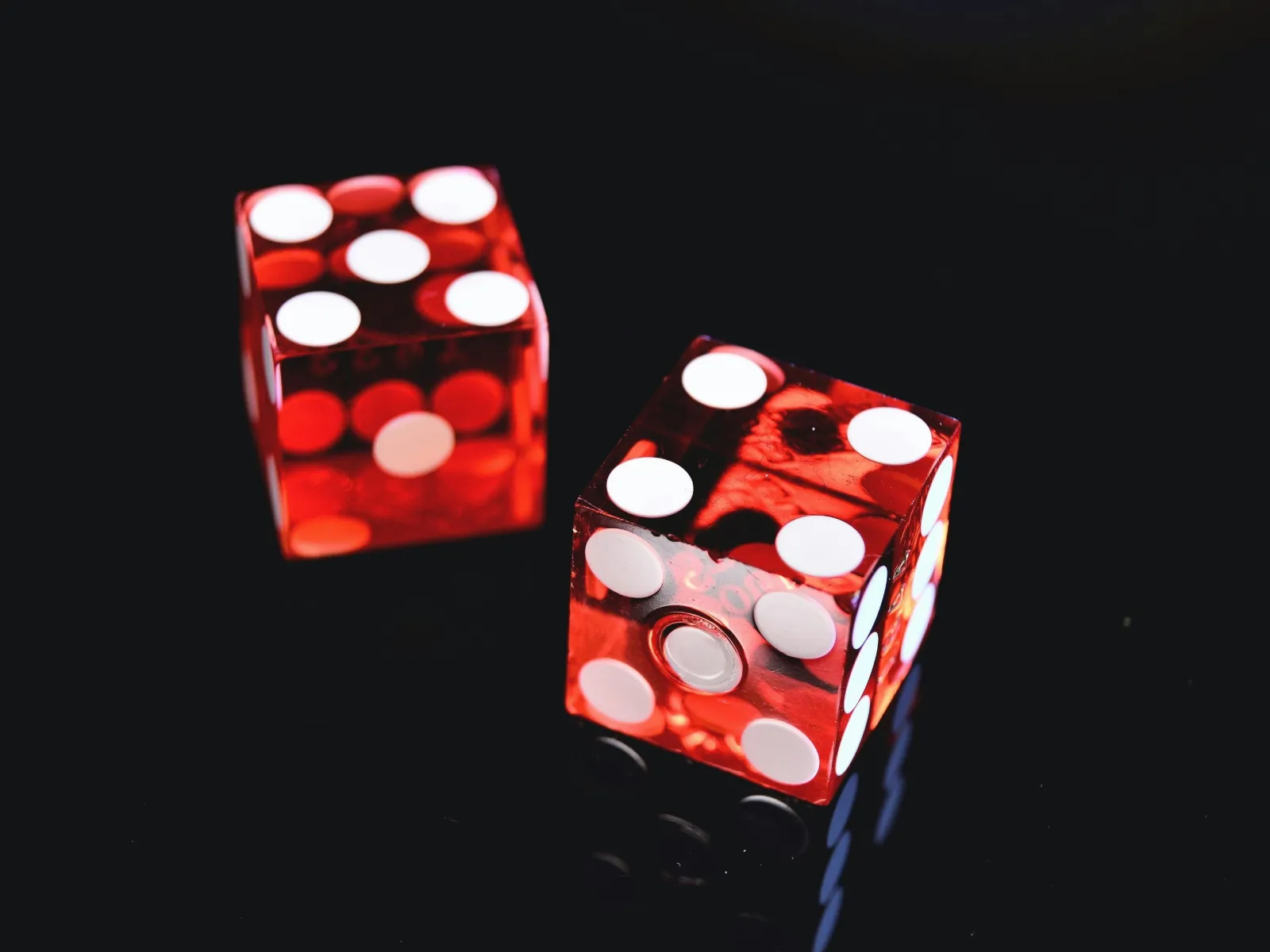 Two red transparent dice with white dots on a shiny black surface showing numbers five and six.