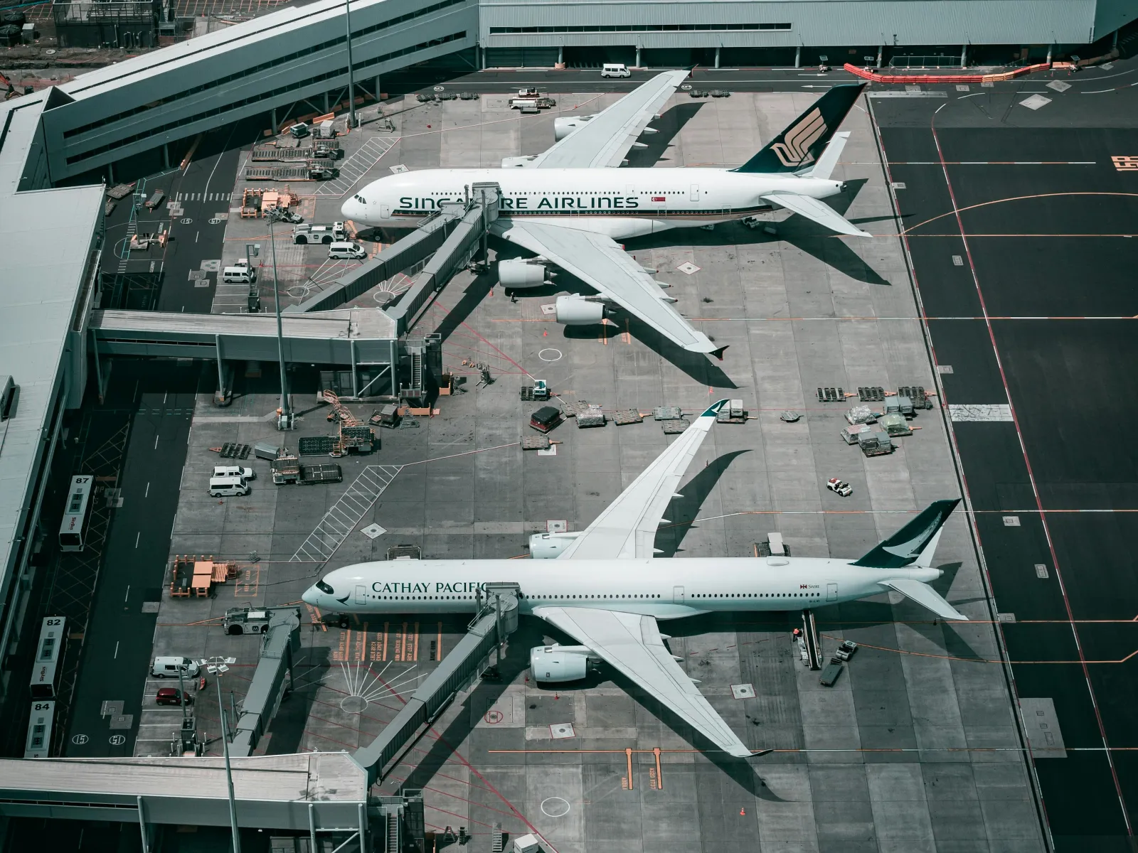 Aerial view of three airplanes from Singapore Airlines, Cathay Pacific, and United parked at airport gates with terminal and parking lot.