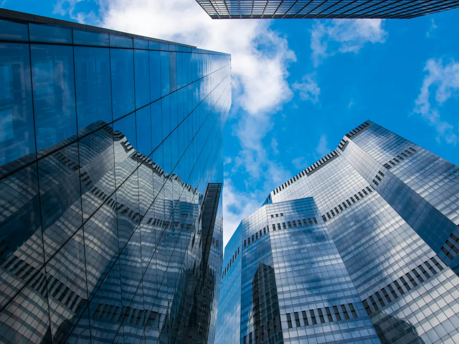 Modern glass skyscrapers reflecting blue sky and clouds in a city business district under bright daylight.
