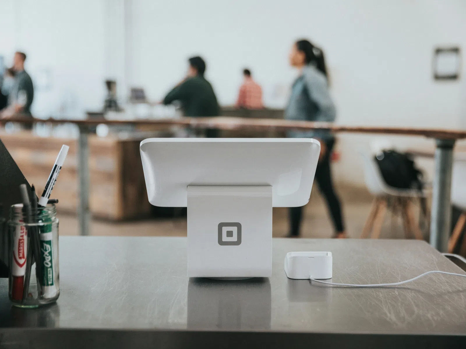 Square point-of-sale system on a store counter with blurred people and wooden furniture in background