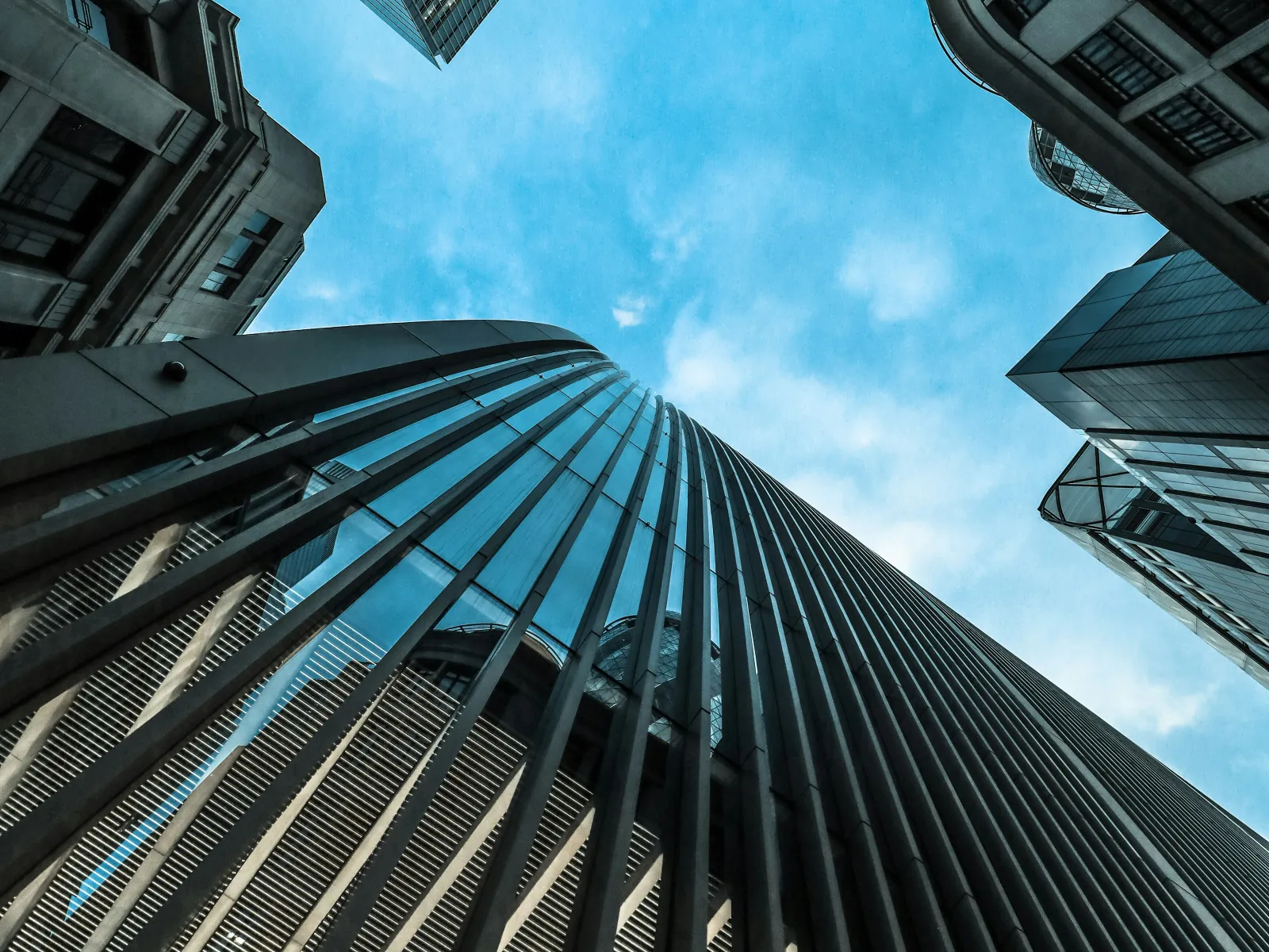 Looking up at modern skyscrapers with blue sky in the background, showcasing architectural lines and glass facades.
