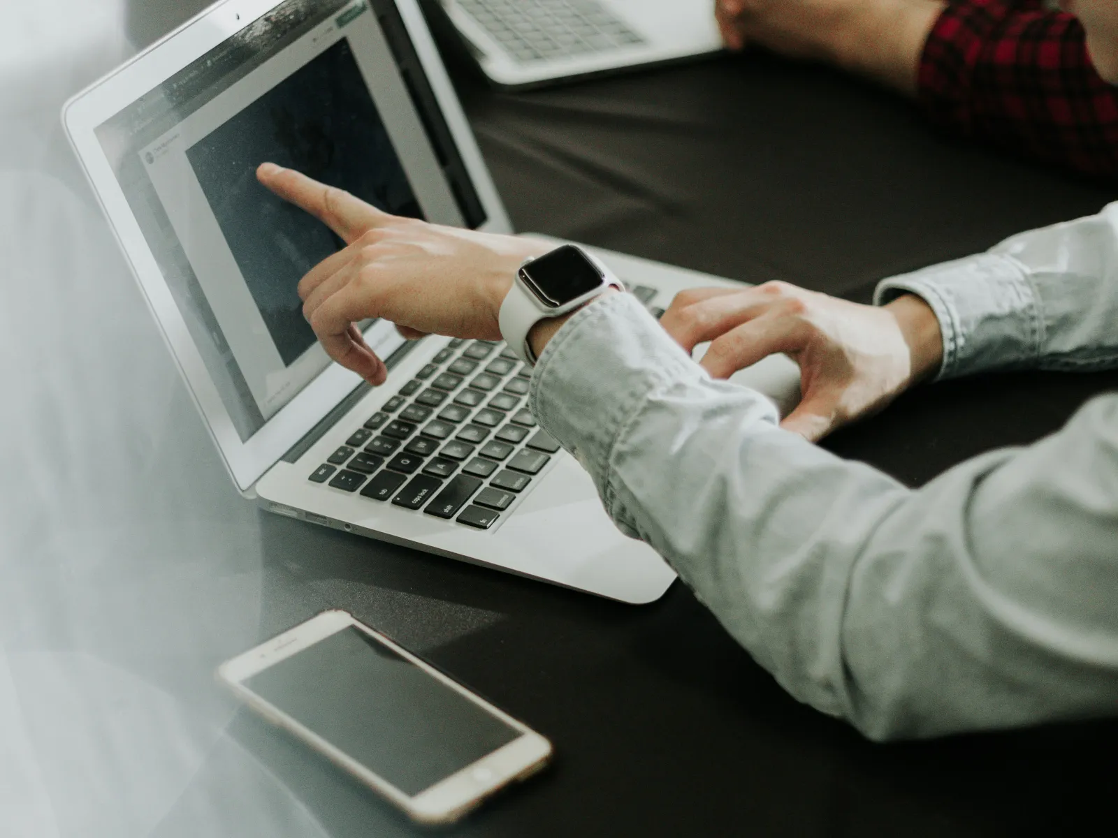 Person pointing at laptop screen during discussion with another person at a black table with smartphones