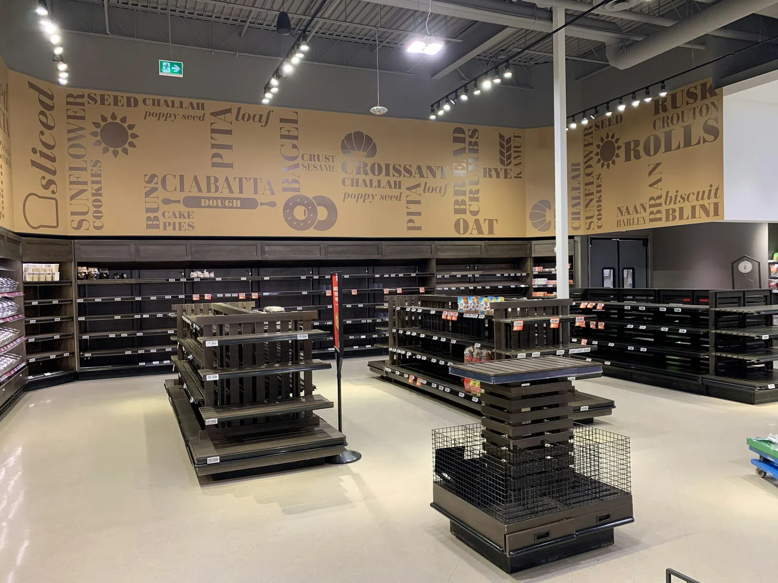 Empty grocery store bread aisle with shelves and bakery-themed wall decor featuring bread-related words and images.
