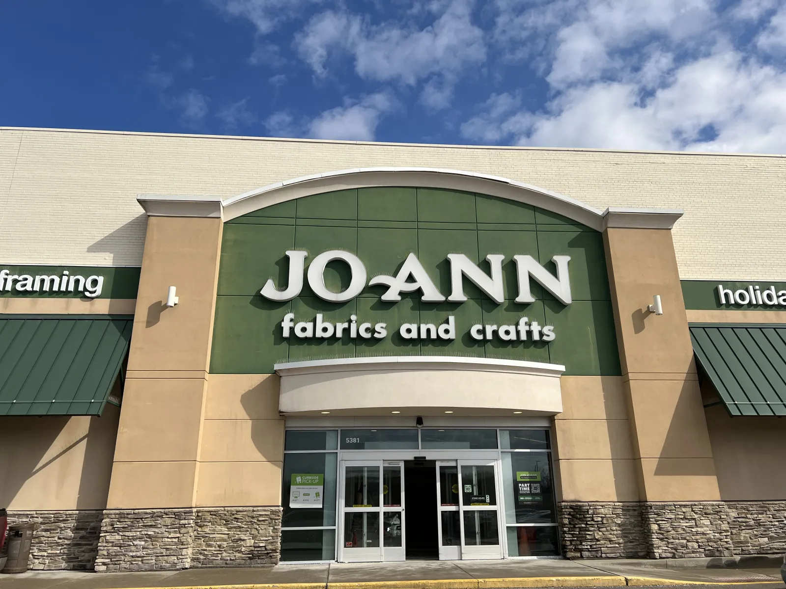 Front view of JOANN fabrics and crafts store with green and beige exterior under a blue sky