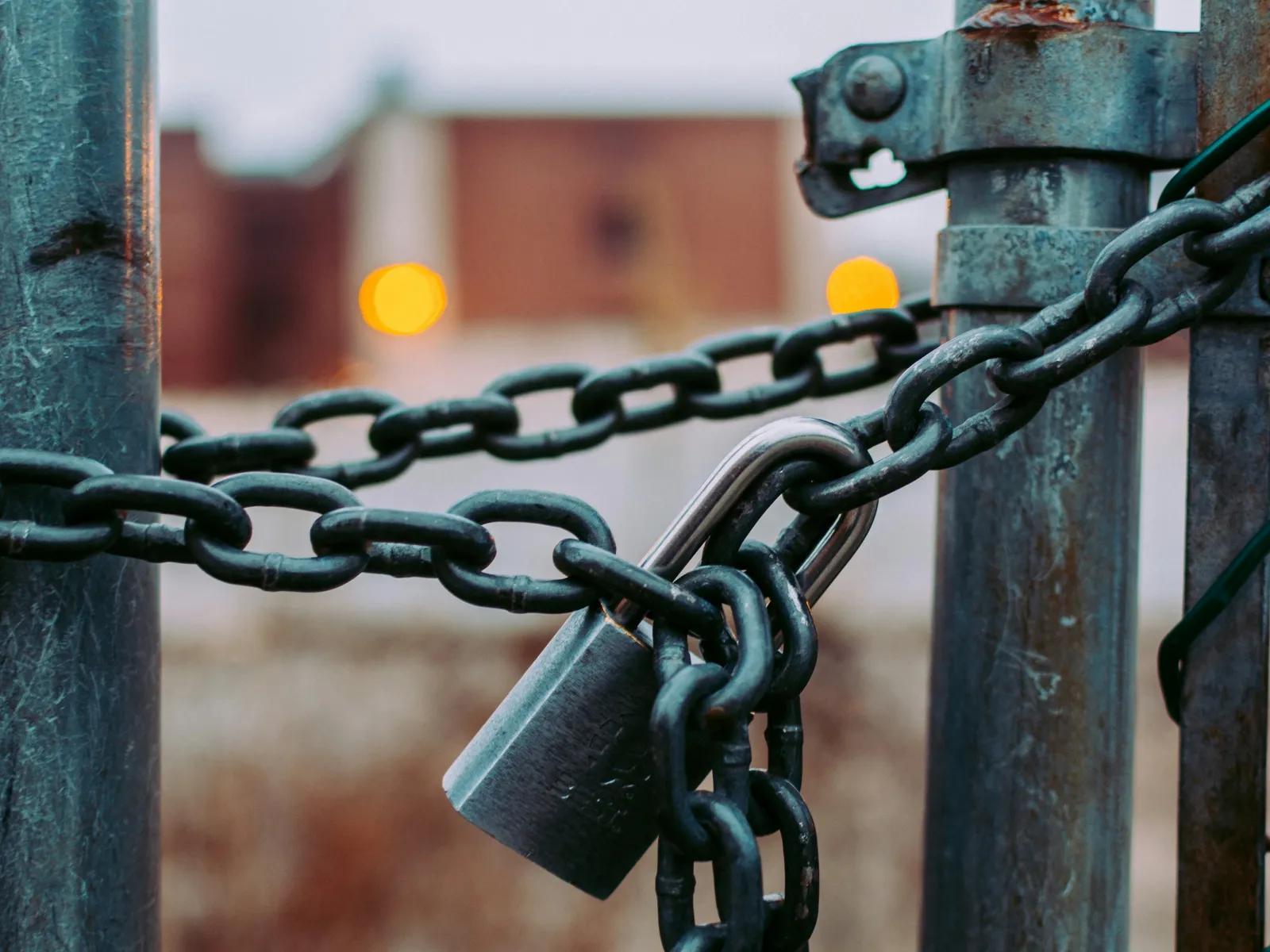 Rusty metal chain and padlock securing a metal gate with blurred background and warm light bokeh.