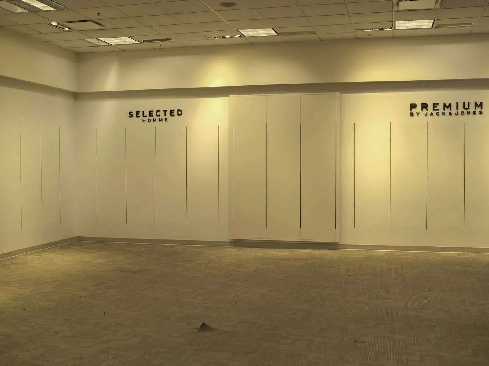 Empty retail space with wall panels labeled SELECTED HOMME and PREMIUM by JACK & JONES under ceiling lights.