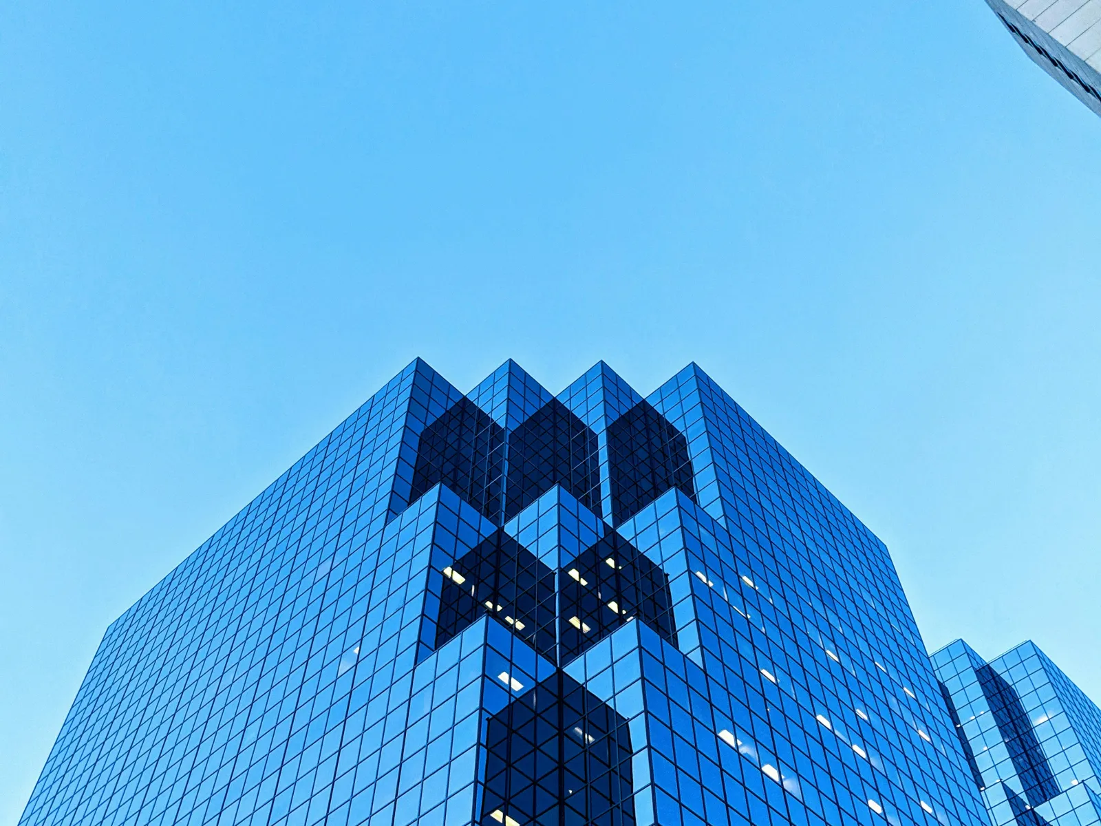 Modern glass skyscraper with reflective blue windows against a clear blue sky, showing geometric patterns.