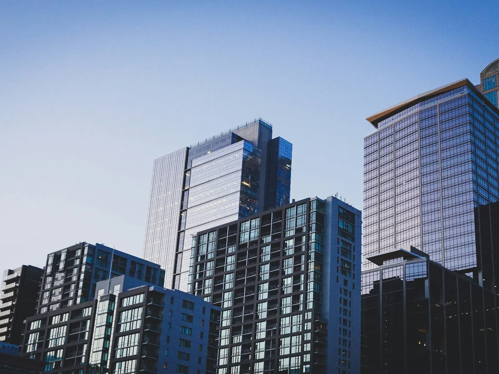 Modern glass skyscrapers and office buildings under a clear blue sky in a city skyline.