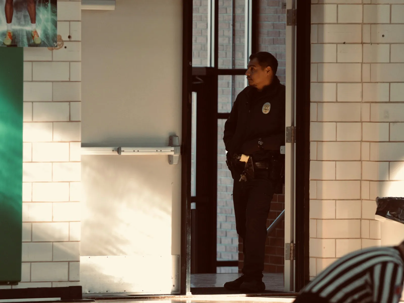 Security guard standing in a doorway of a gymnasium with a basketball court in the foreground