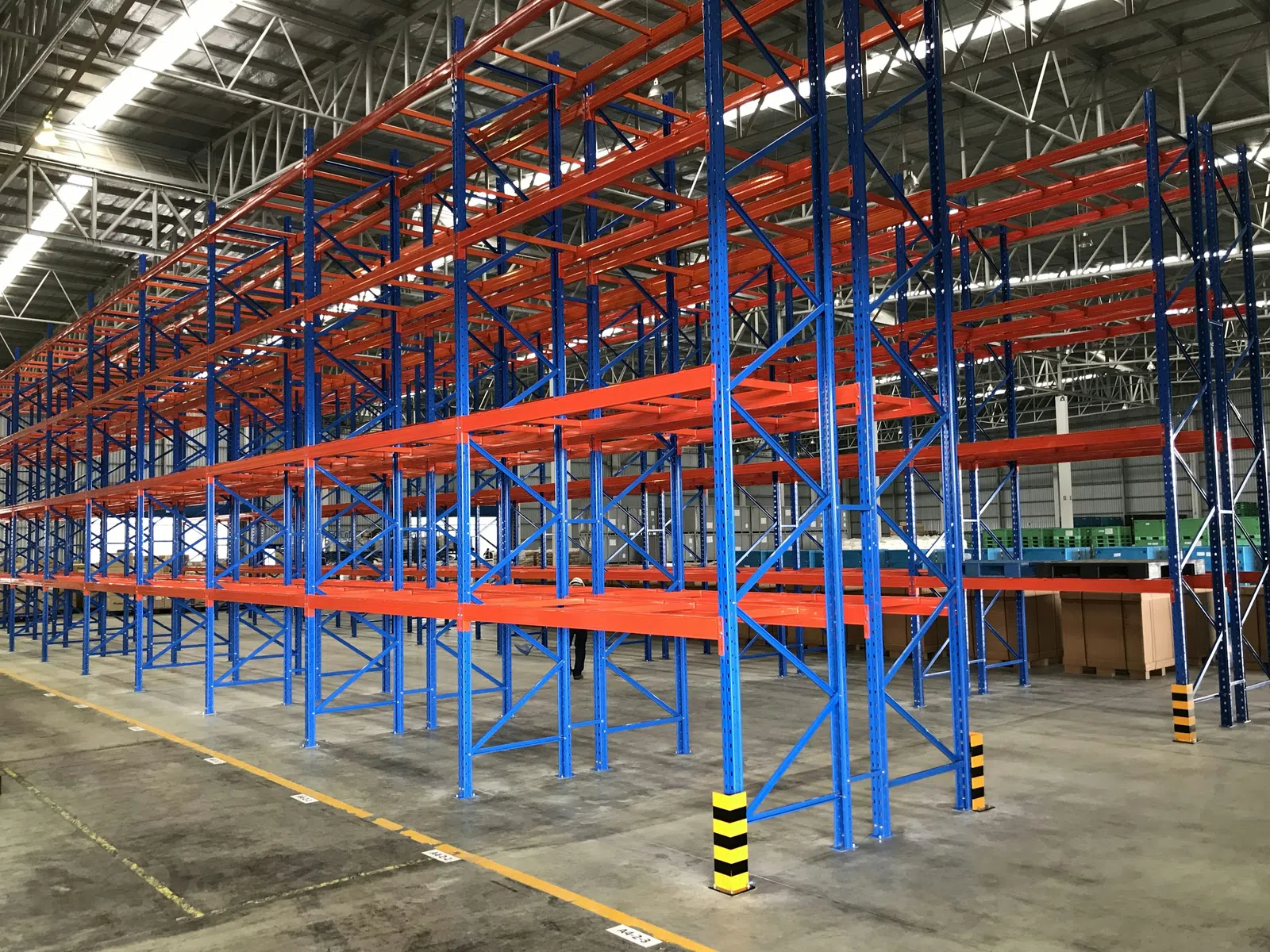 Empty industrial warehouse with blue and orange heavy-duty metal storage racks under a high ceiling
