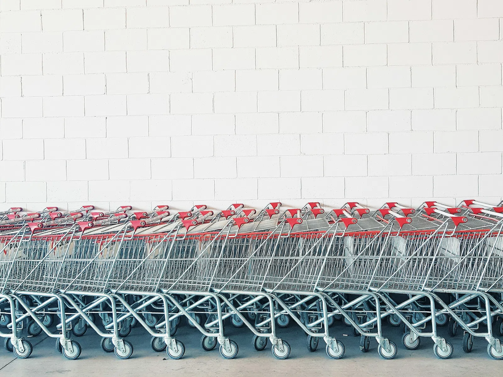 Row of empty metal shopping carts with red handles lined up against a white brick wall.