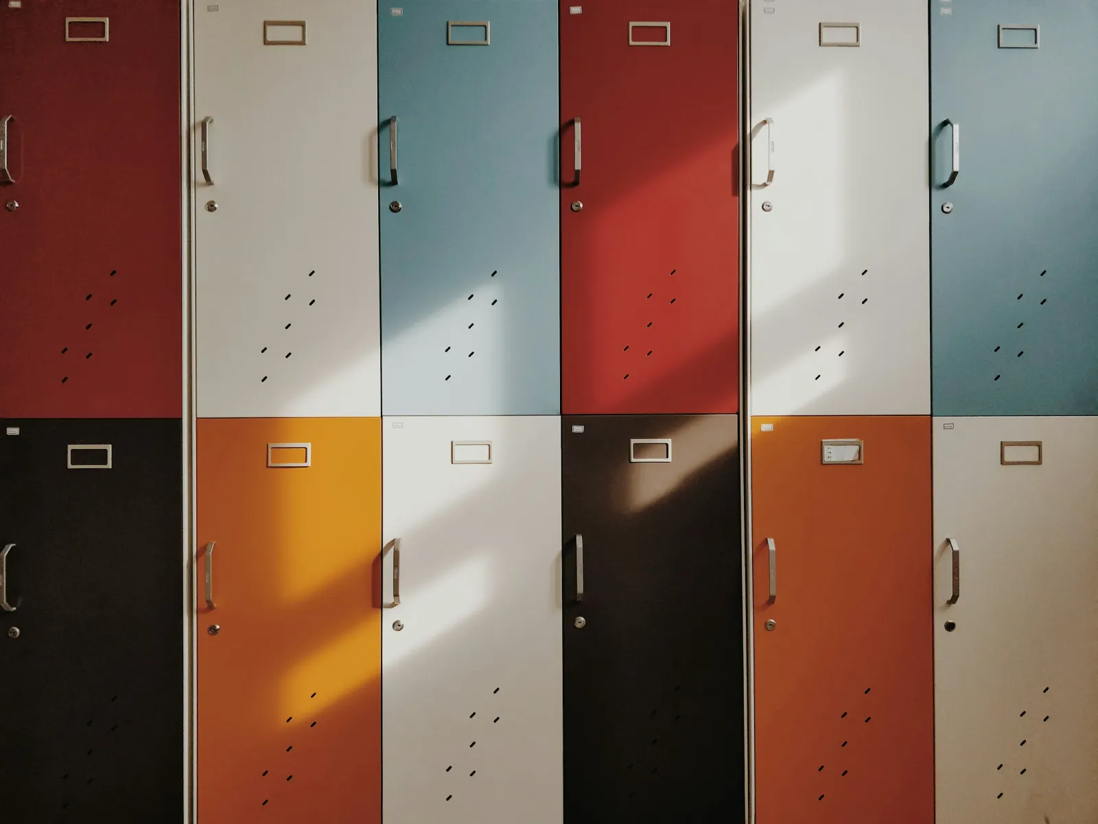 Colorful school lockers arranged in two vertical rows with sunlight casting shadows across the doors.