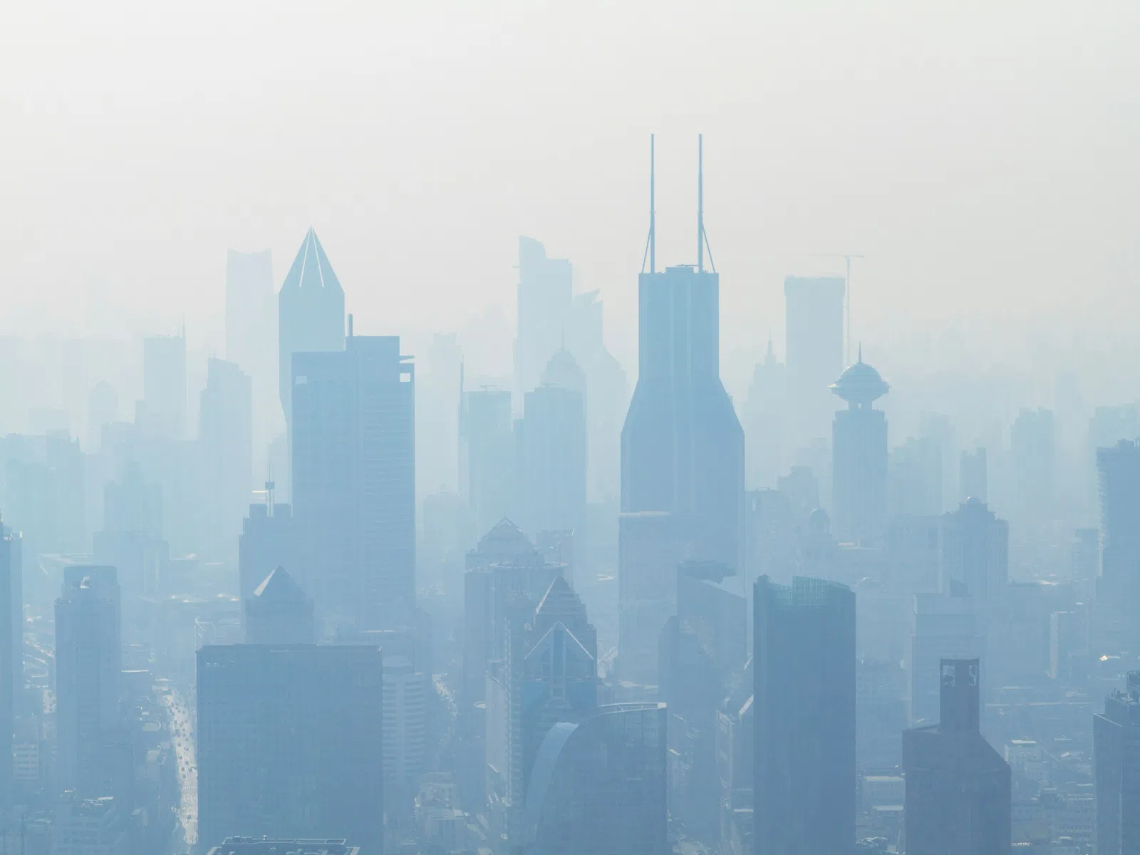Foggy cityscape with modern skyscrapers and high-rise buildings under a hazy sky during daytime.