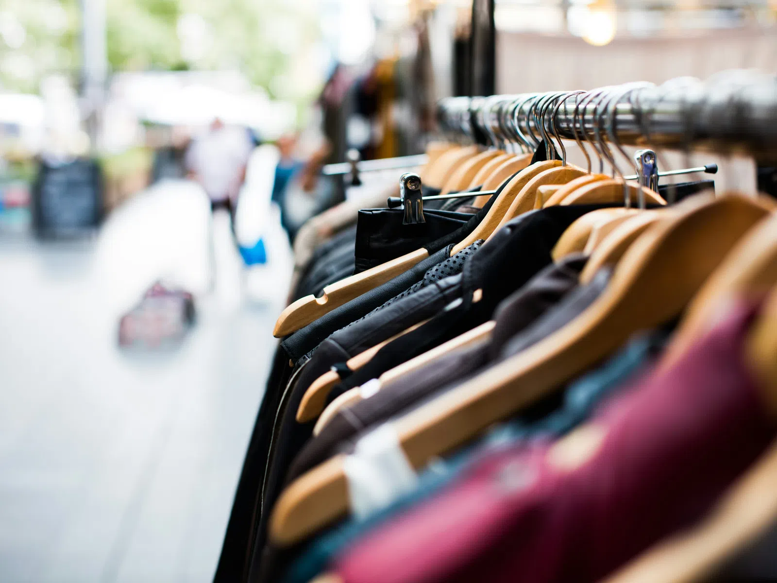 Close-up of various clothes hanging on wooden hangers on a garment rack in a store or market.