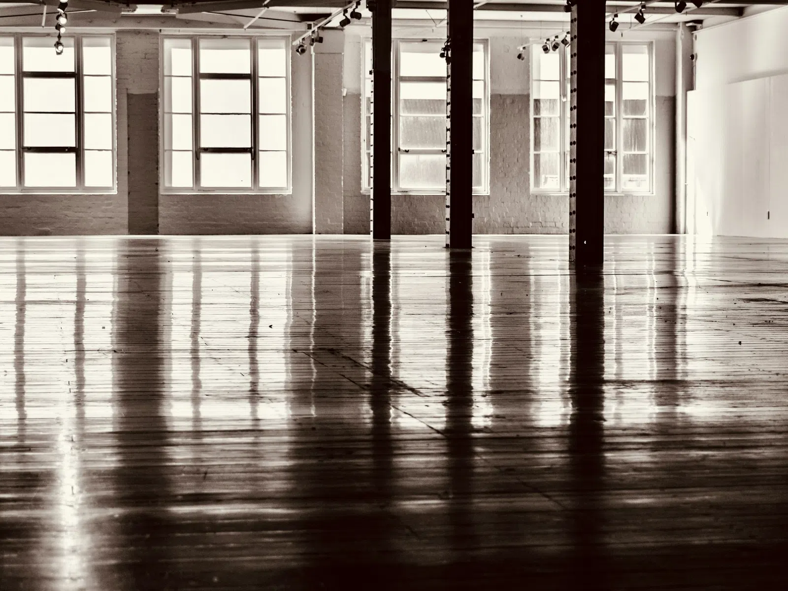 Spacious empty industrial loft with large windows and glossy wooden floors reflecting light