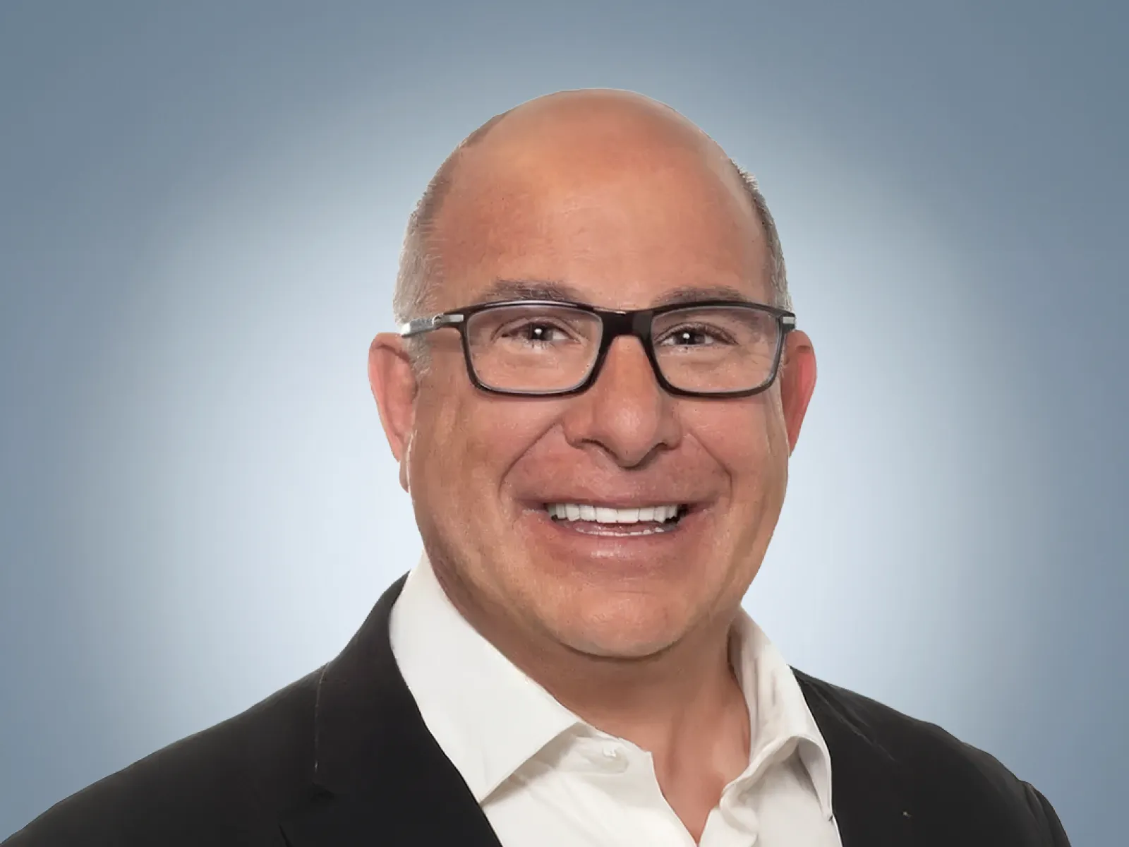 Smiling bald man wearing glasses, white shirt, and black suit jacket against a blue gradient background