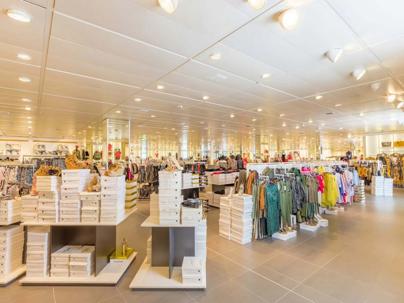 Bright clothing store interior with shoes stacked in boxes and racks of colorful apparel under ceiling lights