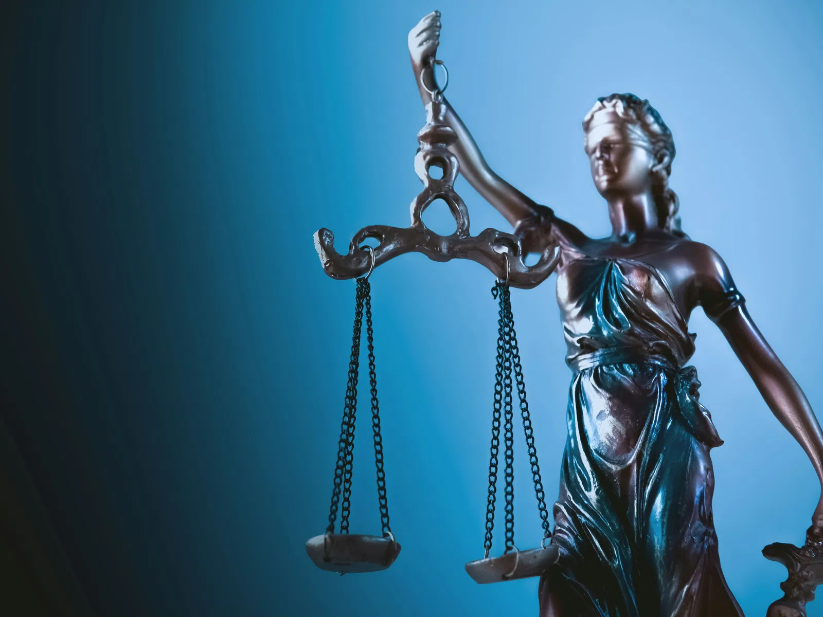 Bronze Lady Justice statue holding balanced scales with a blue gradient background symbolizing law and fairness.