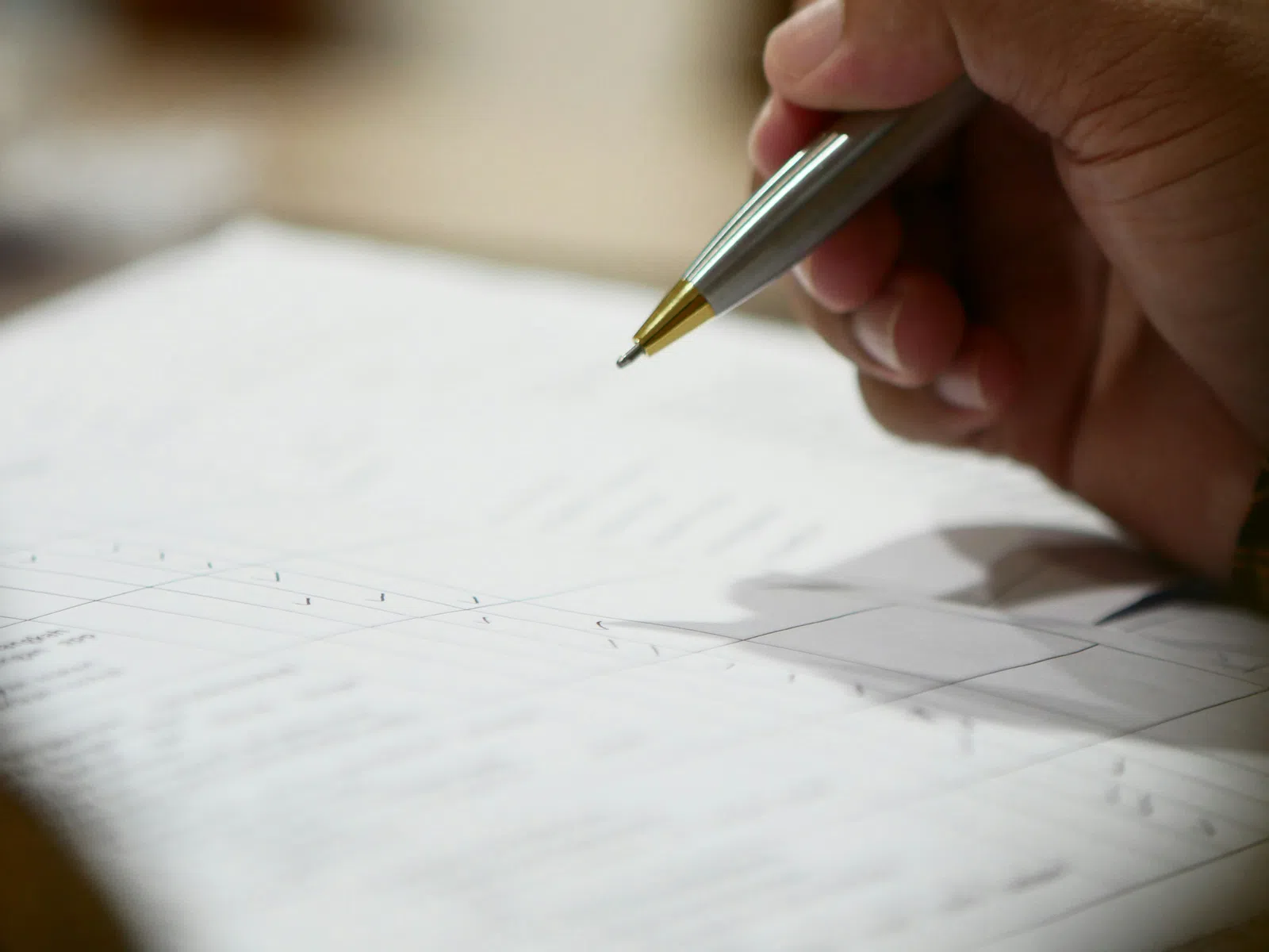 Close-up of a hand holding a pen poised to sign a document with printed text and tables.