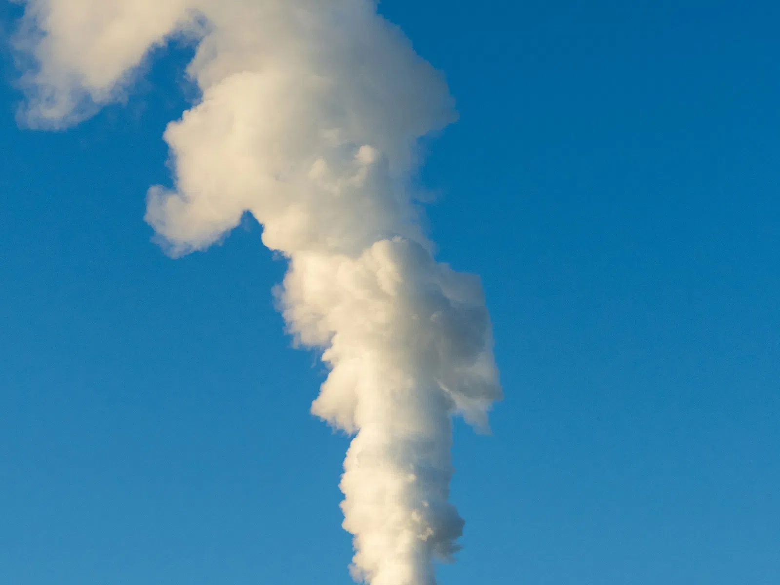 Thick white smoke rising from two factory chimneys against a clear blue sky