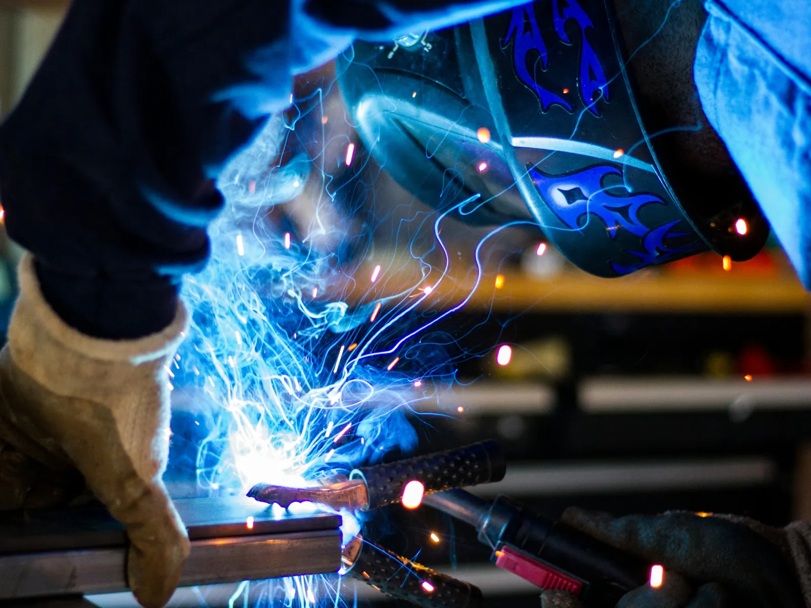 Welder in protective gear welding metal with bright blue sparks and smoke in a workshop setting