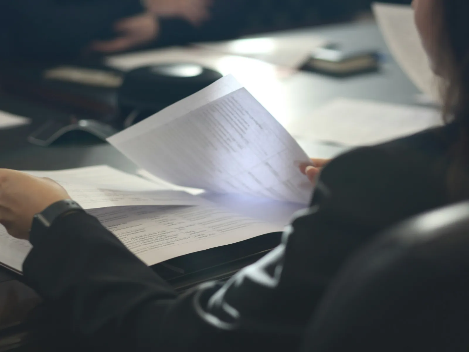 Person in business attire reviewing documents at a meeting table with papers and devices.