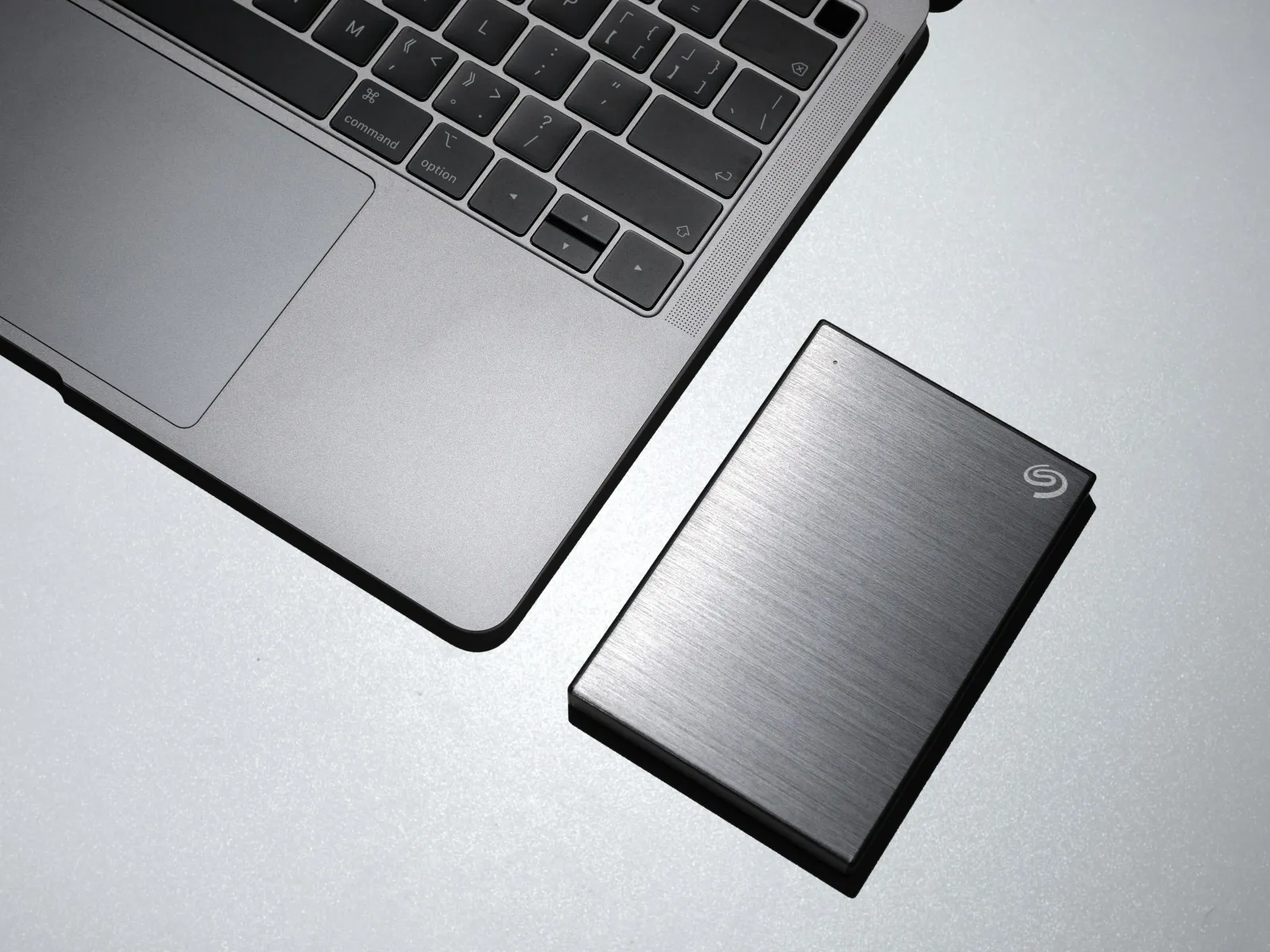 Sleek external hard drive placed next to a laptop on a grey surface for data storage and backup.