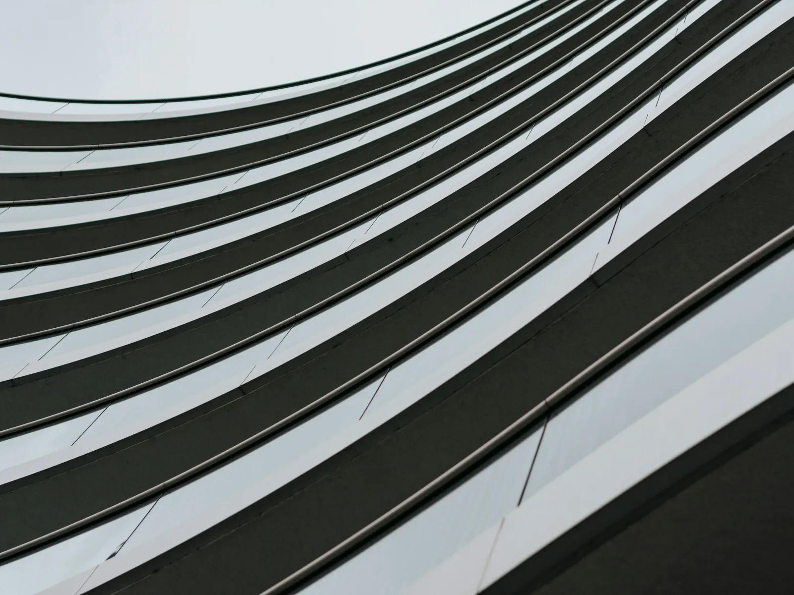 Curved architectural facade with alternating dark and reflective silver horizontal strips creating a wave pattern.