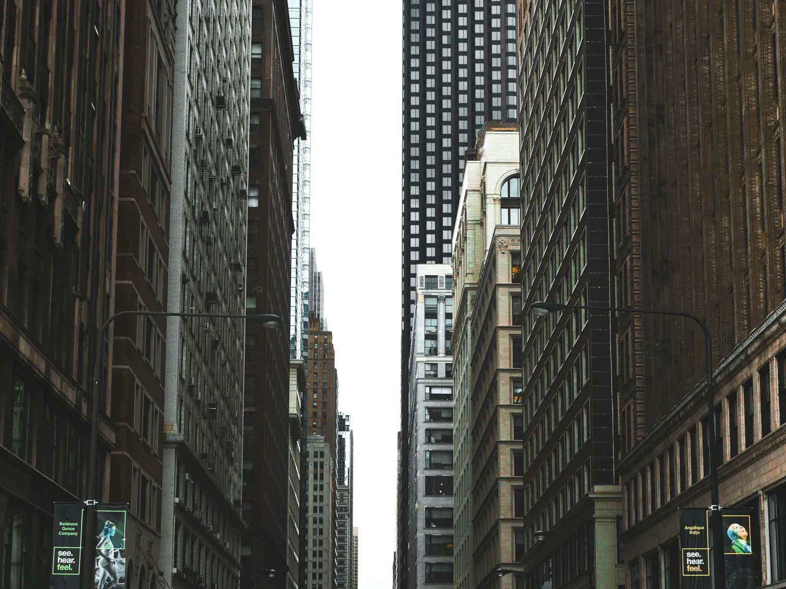 People crossing a busy city street lined with tall buildings under an overcast sky