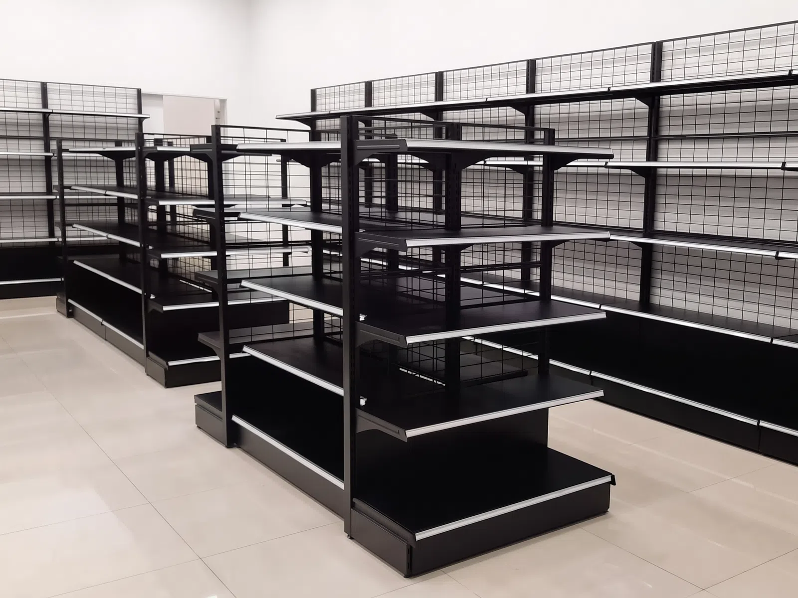 Empty black metal store shelves with grid panels in a clean, well-lit retail space with tiled floors.
