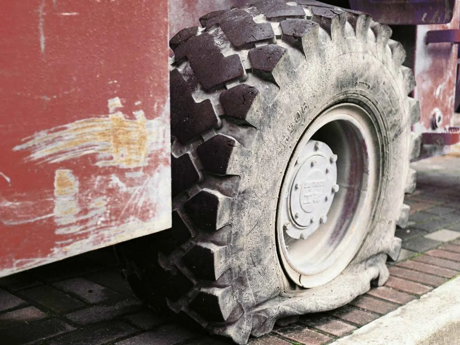 Close-up of a large flat tire on a rugged industrial vehicle with a worn red body and brick pavement.