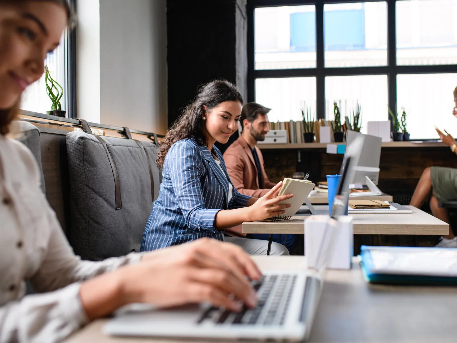 Diverse professionals working in a modern office with laptops, notebooks, and large windows providing natural light.
